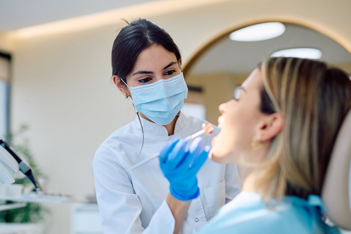 Female dentist wearing mask and gloves performing an oral examination on a woman in a modern dental clinic.