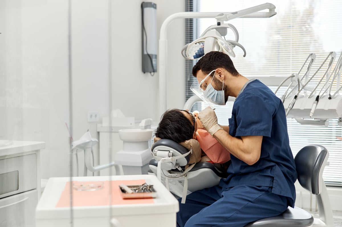 Middle Eastern male dentist examining patient in dental chair during routine checkup in modern dental office.